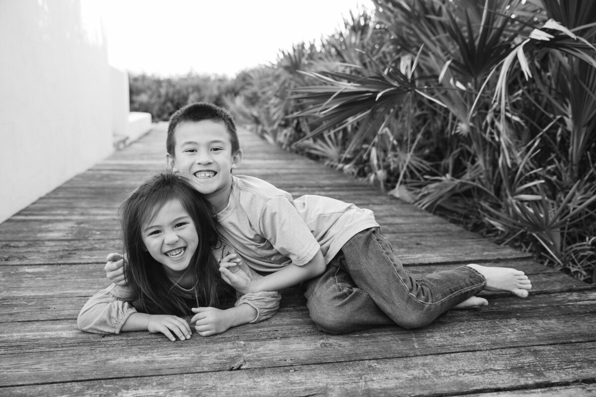 Two siblings laying on a wooden sidewalk smiling