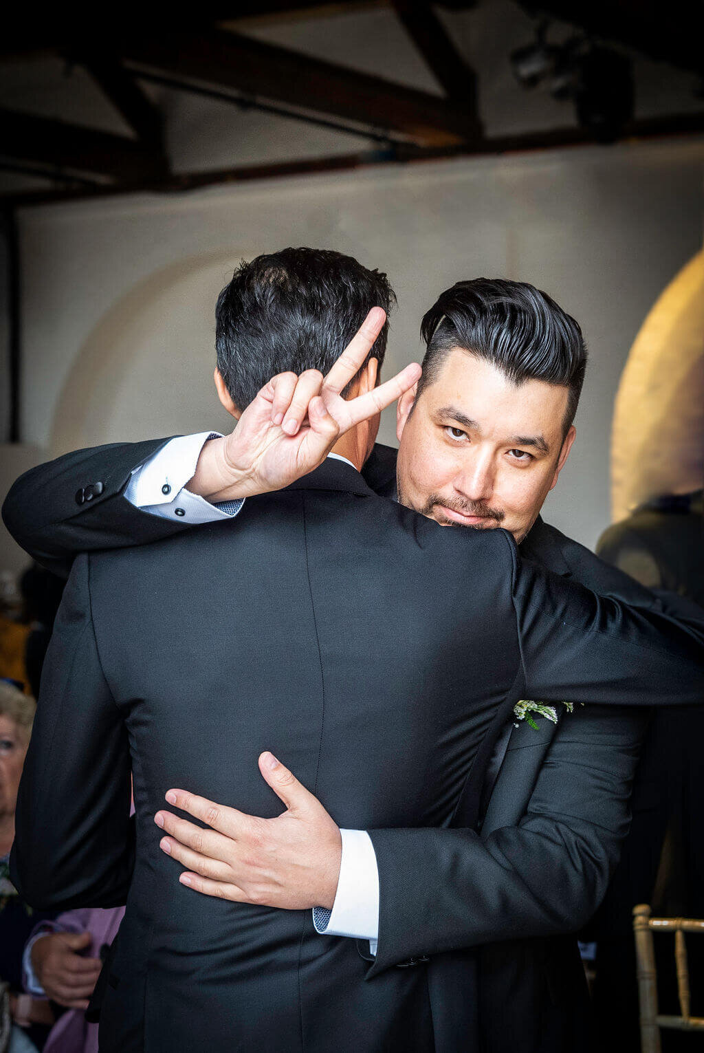 Best Man doing Victory sign to camera hugging the groom