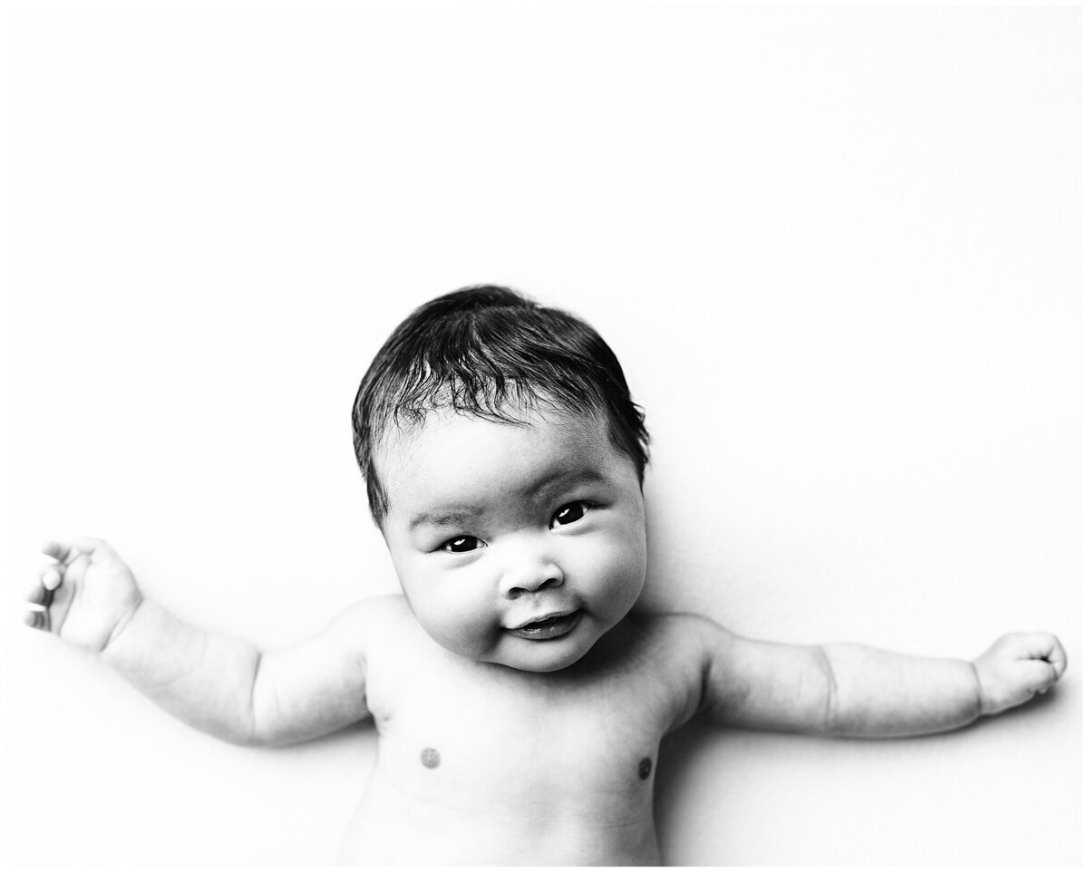 two month old newborn session where the baby girl is laying on her back with arms stretched out smiling at the camera.