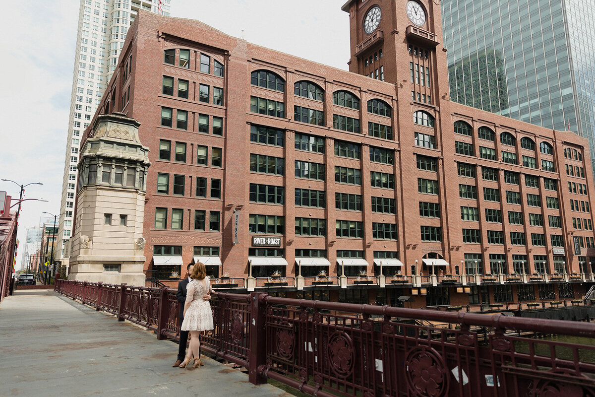 Couple standing on Chicago River bridge with the Reid Murdoch Building in the background.