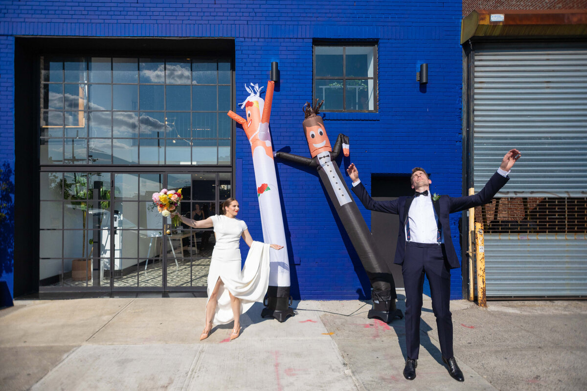 A bride and groom with their hands up imitating inflatables behind them.