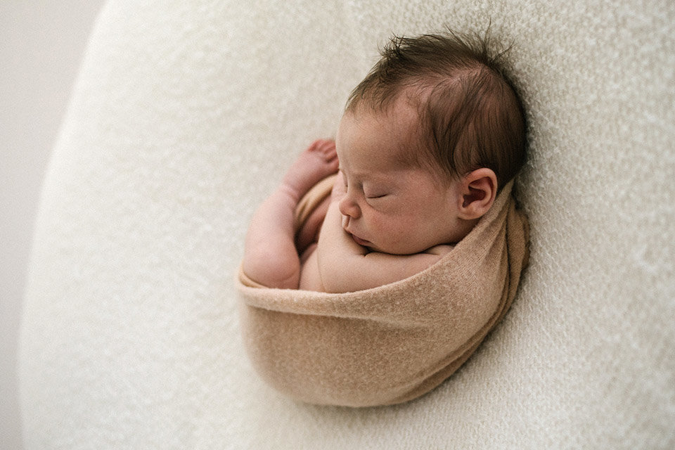 Baby girl curled during newborn session on a white blanekt