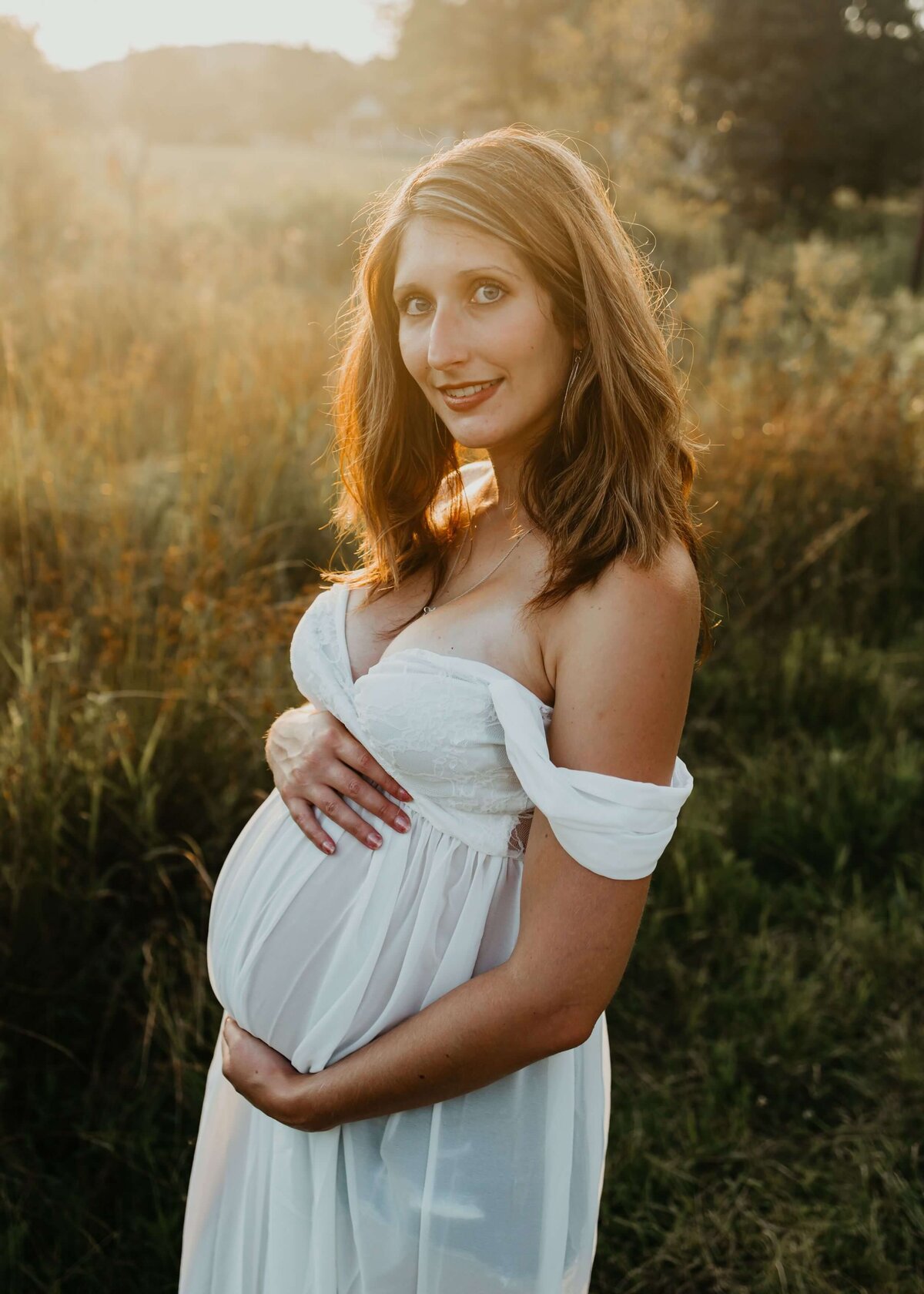 A pregnant woman in a white dress captured by a Pittsburgh maternity photographer standing in a field.