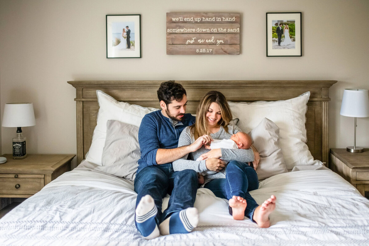 Young family, looking down at their newborn baby while sitting in bed