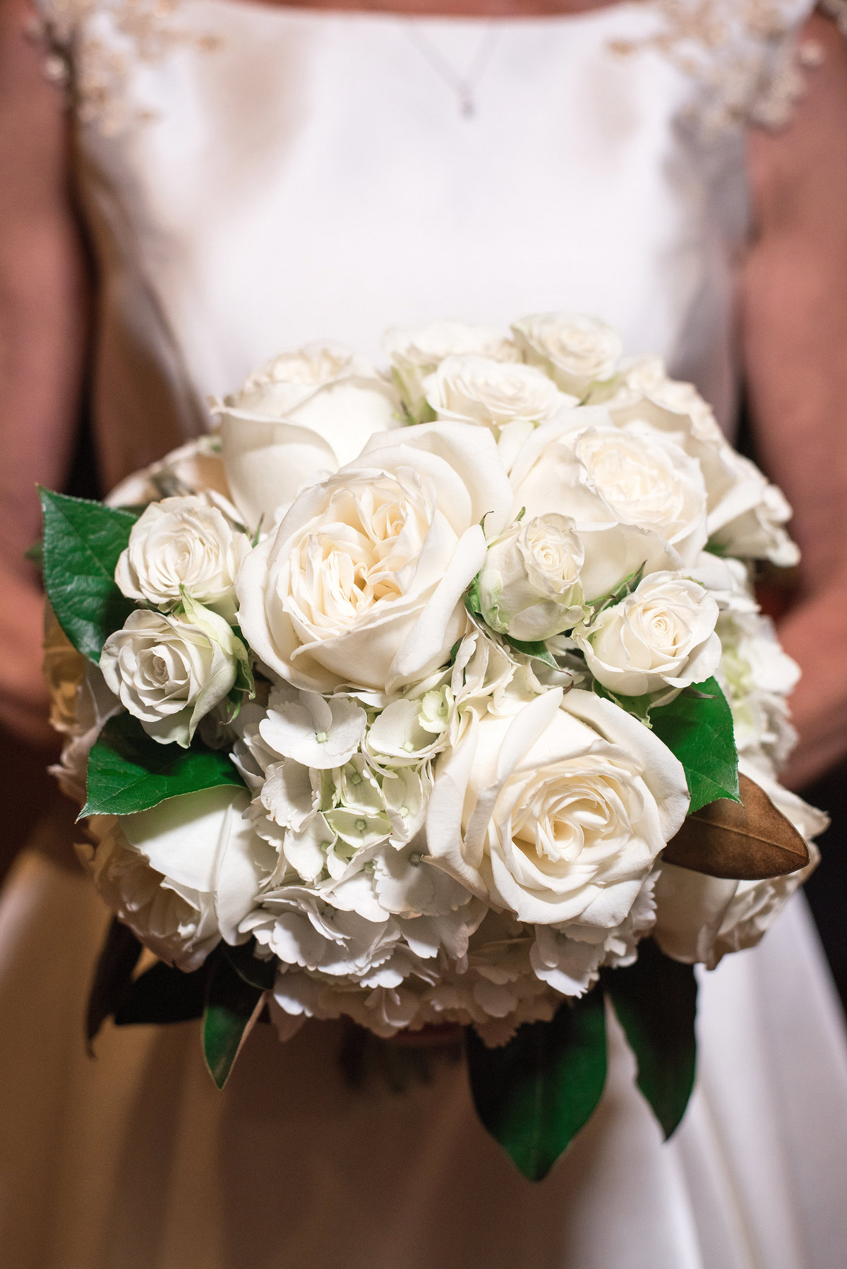 Detail image of a large round white bridal bouquet made up of white roses, white hydrangea, white tea roses and lemon leaf.