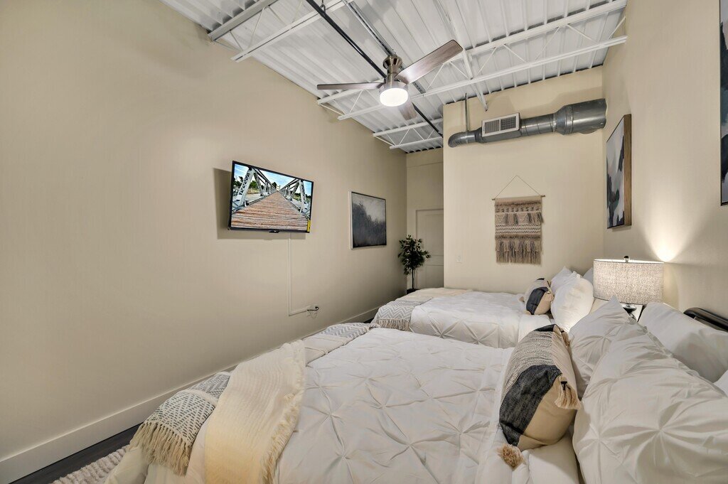 Bedroom with two queen beds and smart TV in this 2 bedroom, 2.5 bathroom luxury vacation rental loft condo for 8 guests with incredible downtown views, free parking, free wifi and professional decor in downtown Waco, TX.