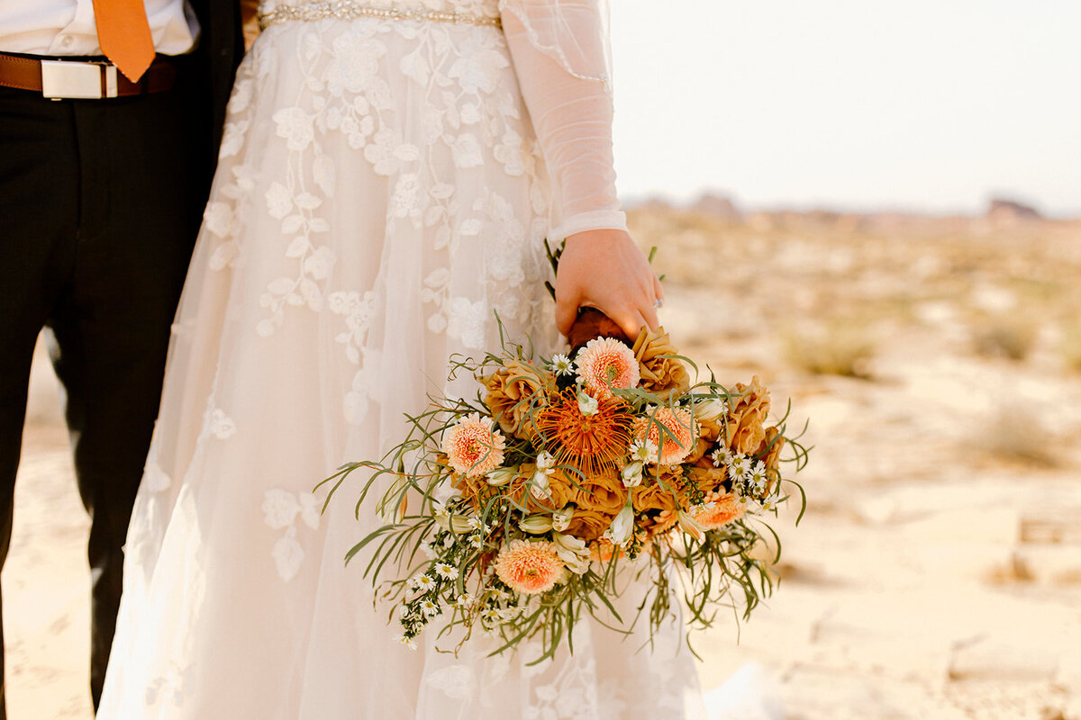 a bride holding an orange and yellow flower bouquet