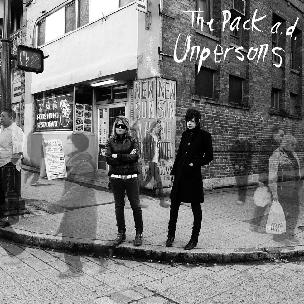 Album Cover The Pack AD Title Unpersons black and white photo duo standing on street corner faded images of people walking down street surrounding them