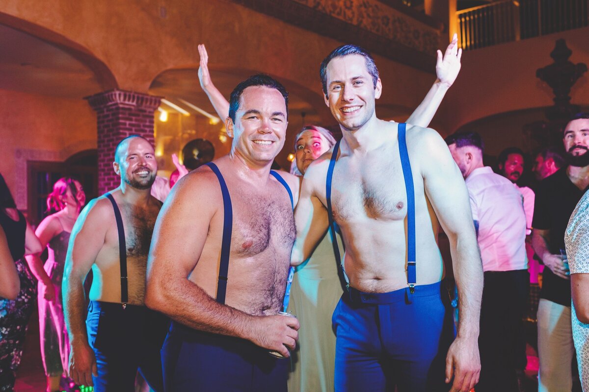 Groomsmen with shirts off on dance floor at wedding