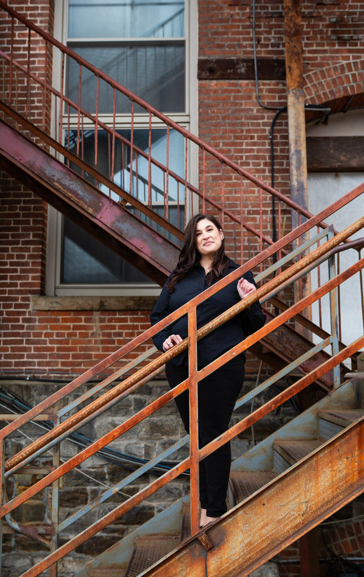 A-woman-smiles-on-rusty-stairs-during-her-branding-photoshoot-in-industrial-hampden