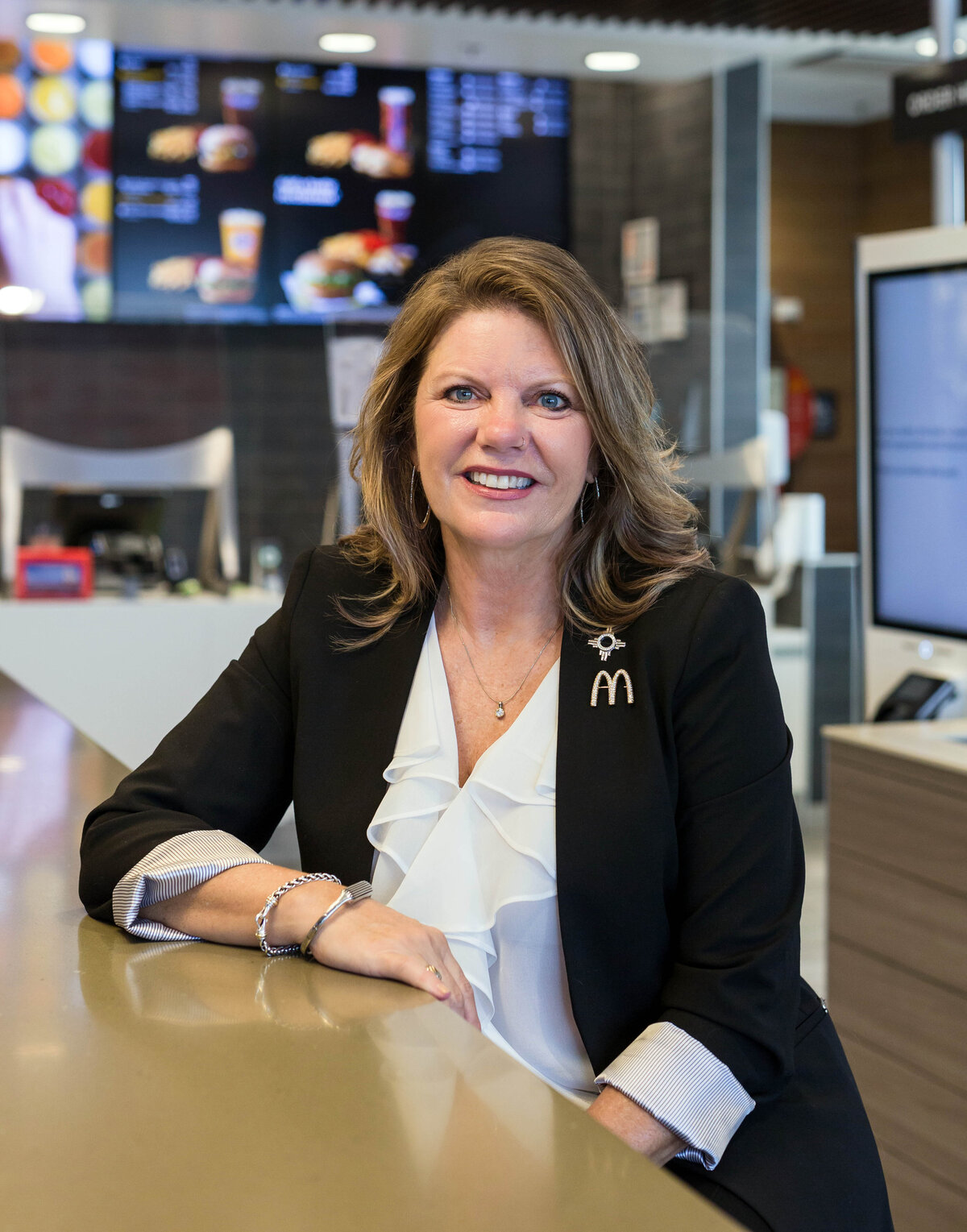 Woman headshot on location inside a McDonald's restaurant where woman is wearing a black suit jacket and white ruffled blouse and smiling at the camera