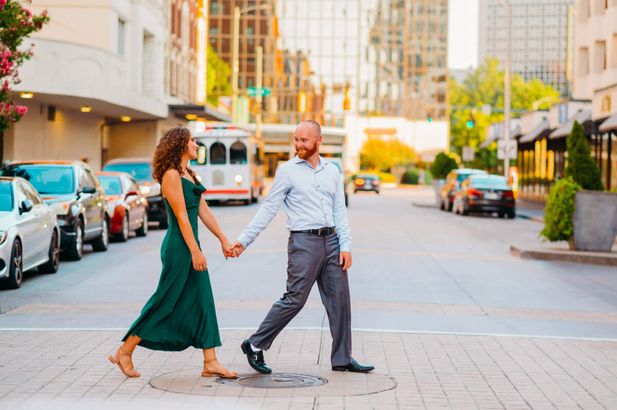 photo of a man in dress pants holding his fiacnee's hand and guiding her across the street