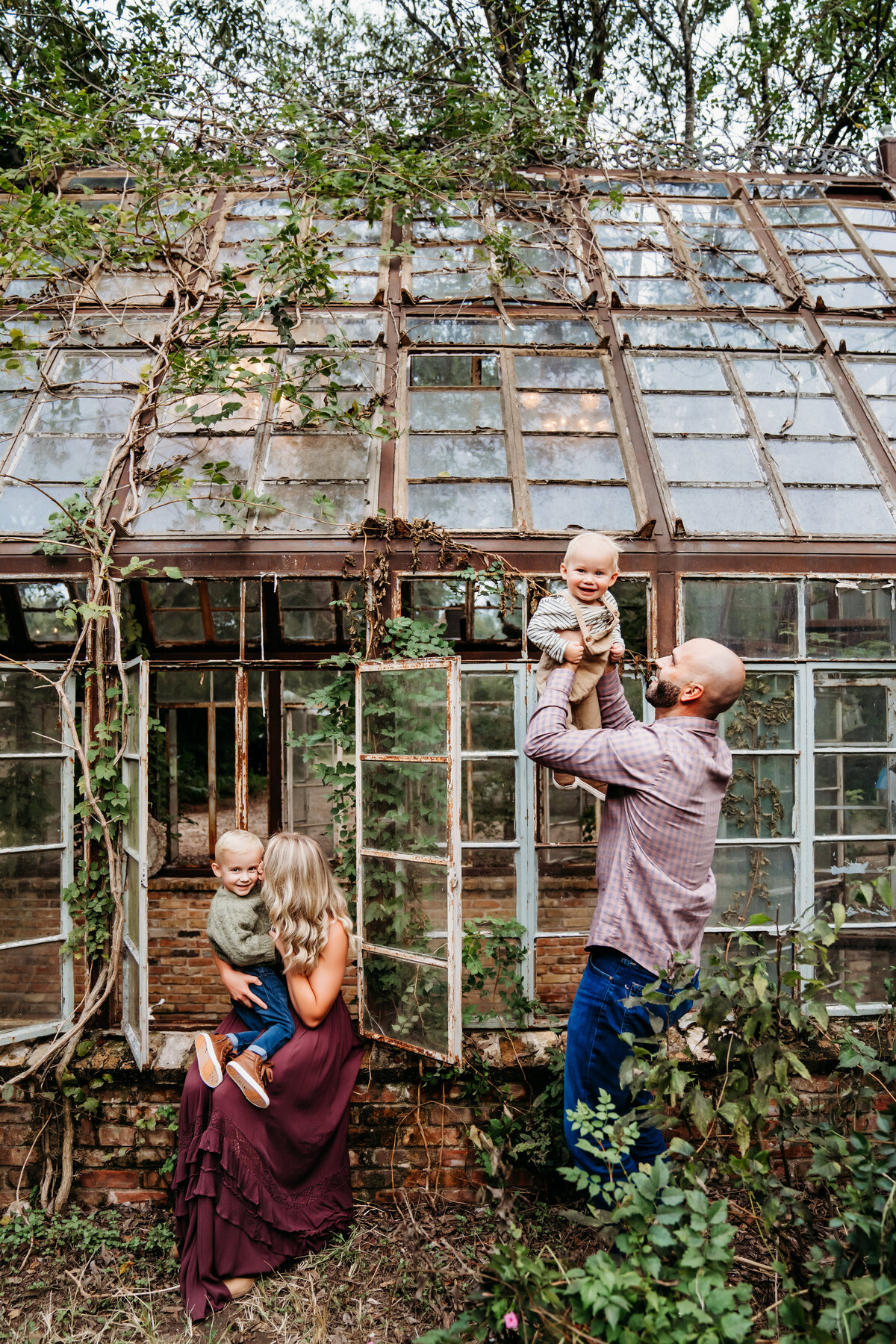 Family Photographer, a small family admires each other outside a green house covered in ivy