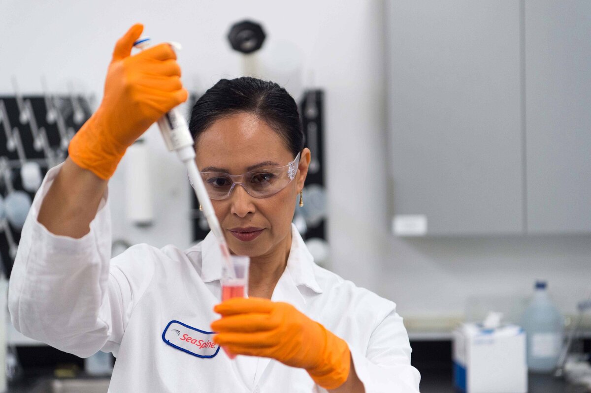 Scientist uses a pipette to drop red liquid into test tube to show precision and care put into research and development process for Seaspine marketing