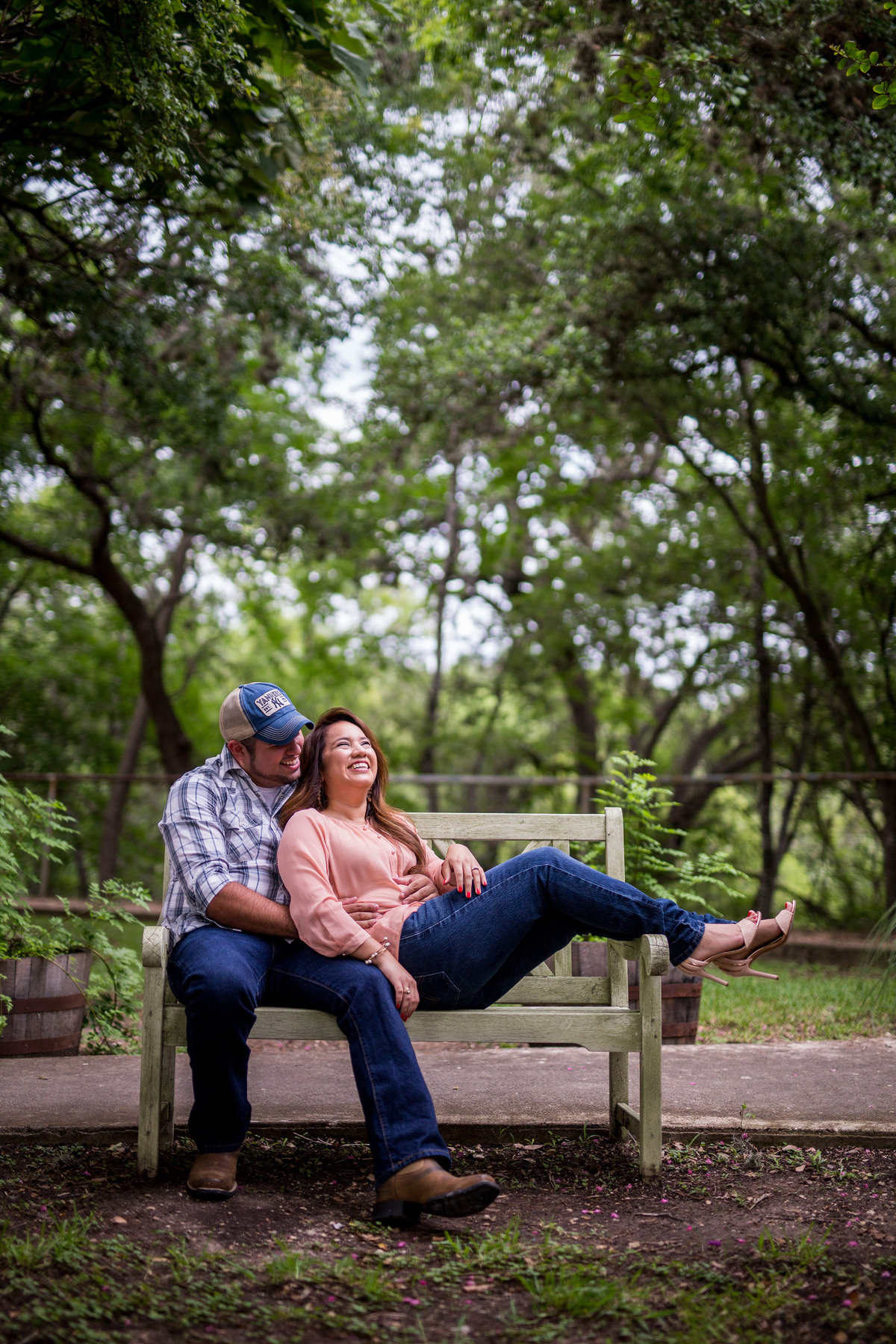 A man and woman in love and laughing while sitting on a bench in Gruene, Texas while on their engagement photo shoot.