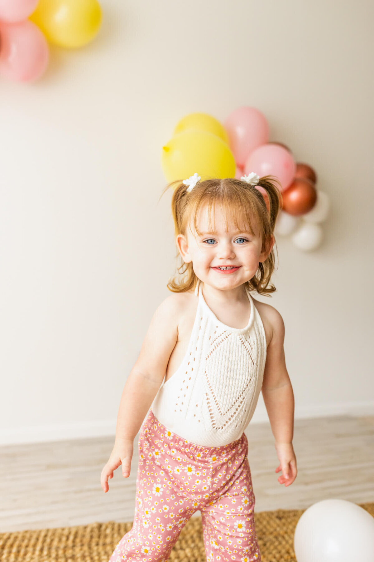 Toddler girl dresses in bell bottoms and a lace romper standing with colorful balloons and smiling
