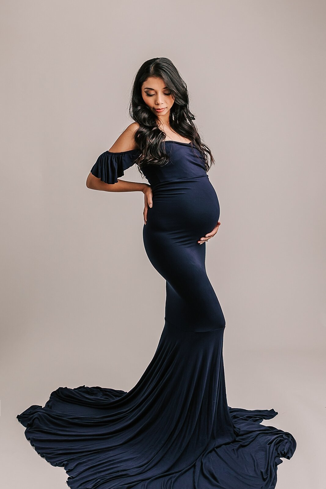 mom wearing blue dress looking down in studio maternity photography portrait
