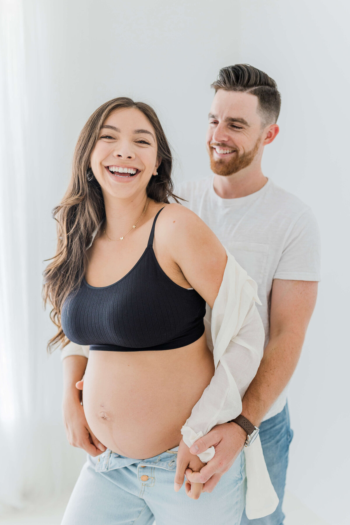 Maternity couple laughing together during their maternity photoshoot in studio in folsom ca with photographer bendel photography