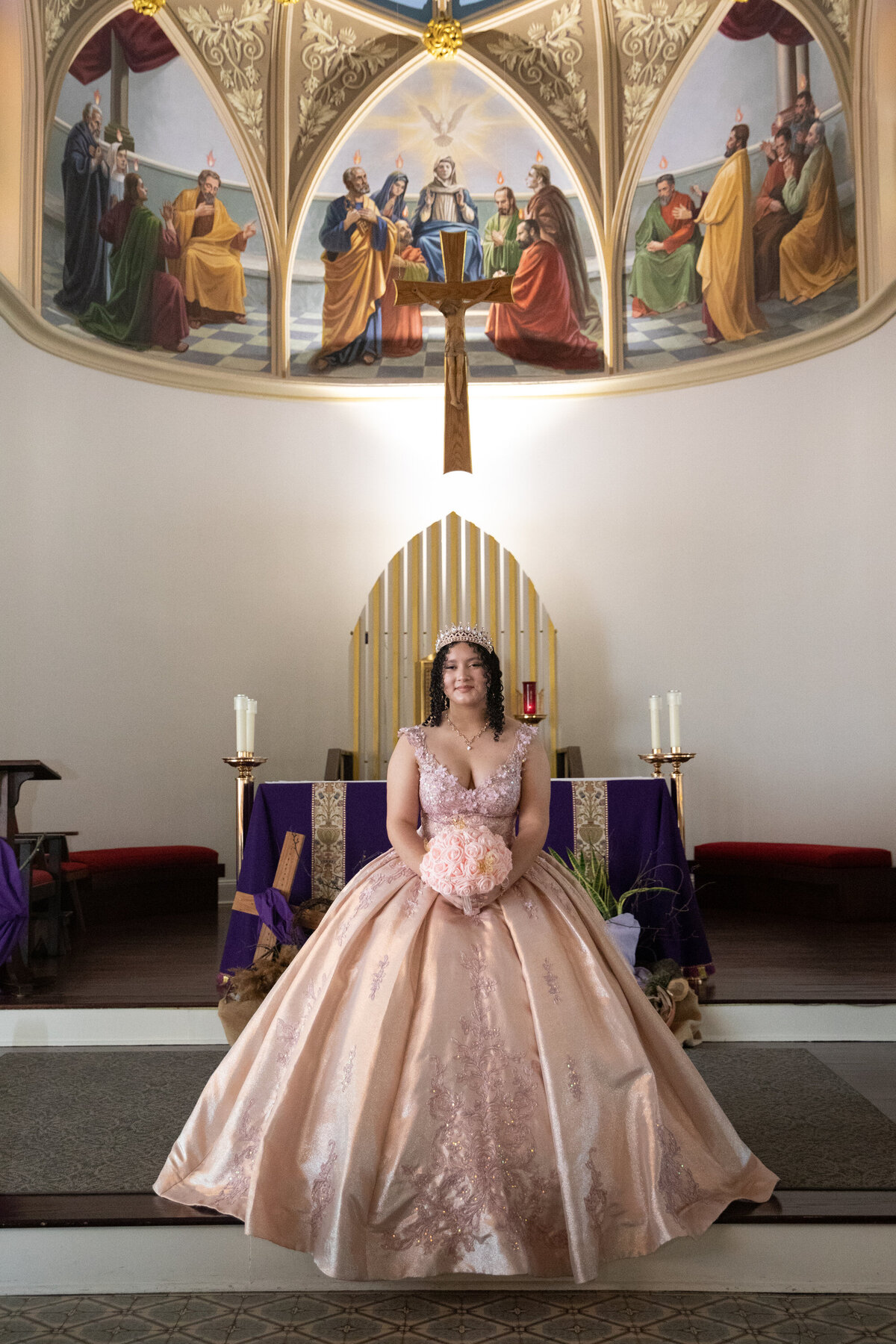 young Mexican-American teenage girl in crown and pink ballgown with bouquet poses on altar Saint Peter's Church Haverstraw quinceanera photographer Rockland County Milestone Images