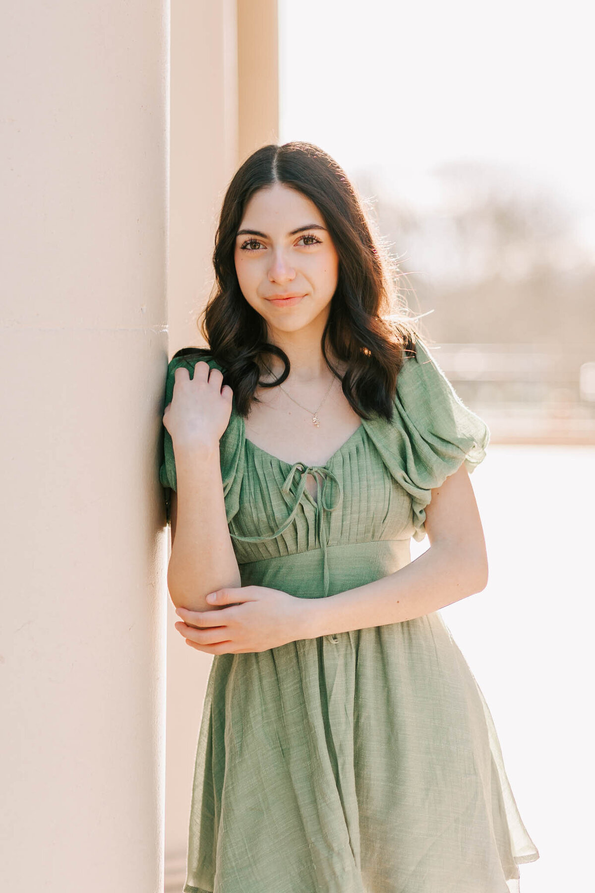 A young woman with brown hair in a green dress leans against a column at OSU campus in Corvallis, OR. She's posing for senior portraits with Jen White Photography