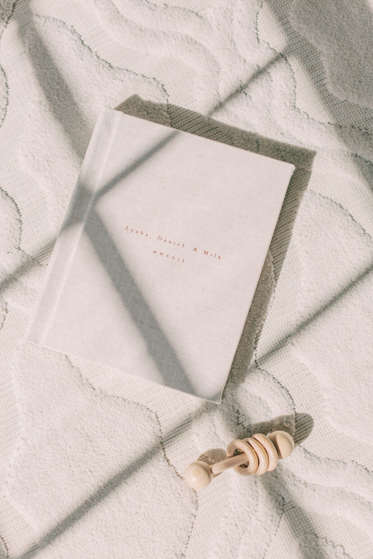 Natural linen album lying on the floor with a wooden rattle