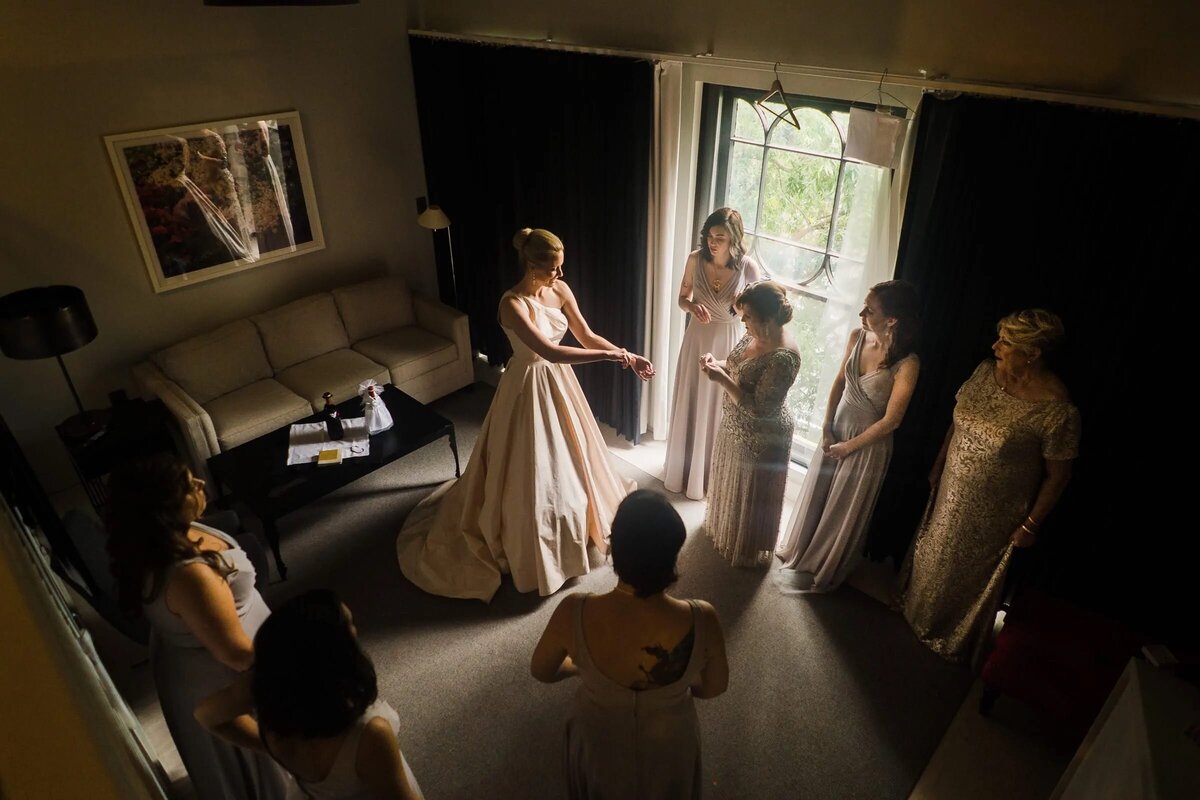A bird's-eye view of a bride surrounded by her bridesmaids in a softly lit room