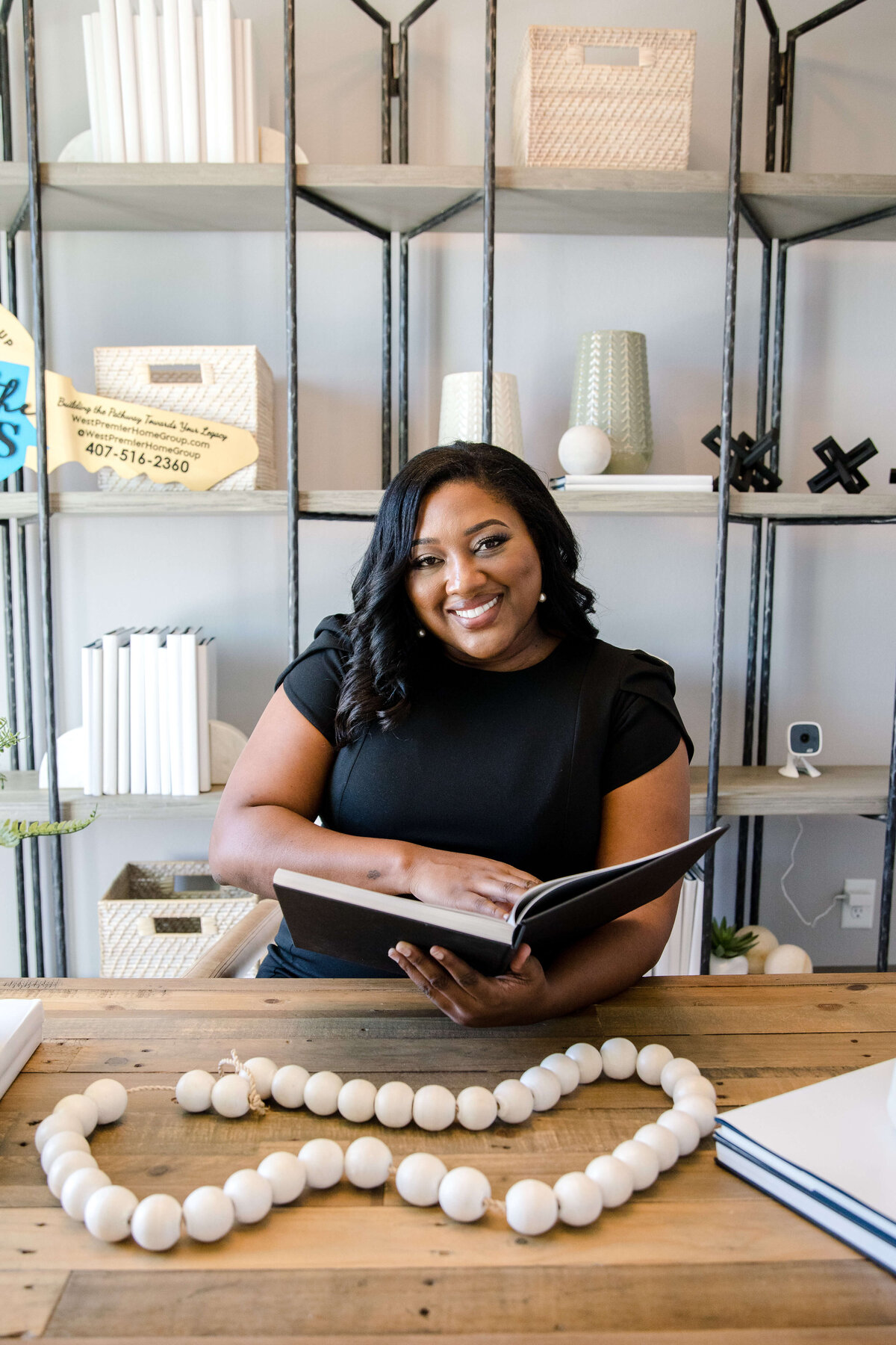 black owned business brand photography with woman sitting at a wooden desk and holding a portfolio with shelves behind her captured by commercial photographers