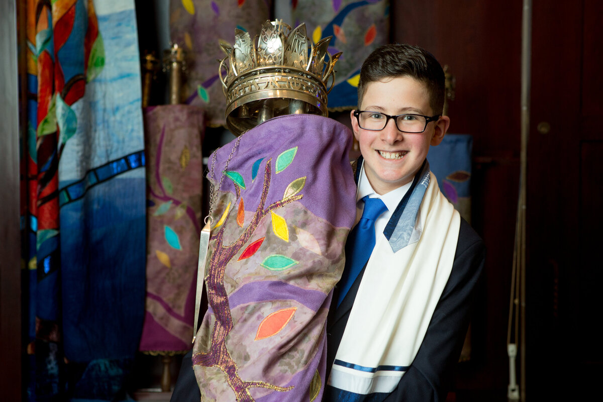 A teenage boy holds a Torah scroll posing for bar mitzvah photographer Orangetown Jewish Center Milestone Images