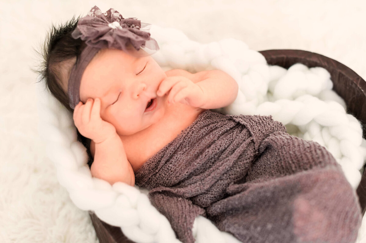 An Edmonton newborn baby girl in a purple wrap resting in a heart shaped bowl at Cynthia Priest's photography studio in Edmonton