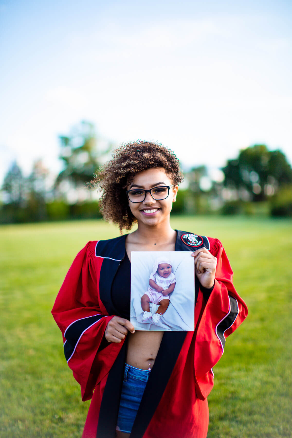 Girl in her graduation gown holding an image of herself as a child