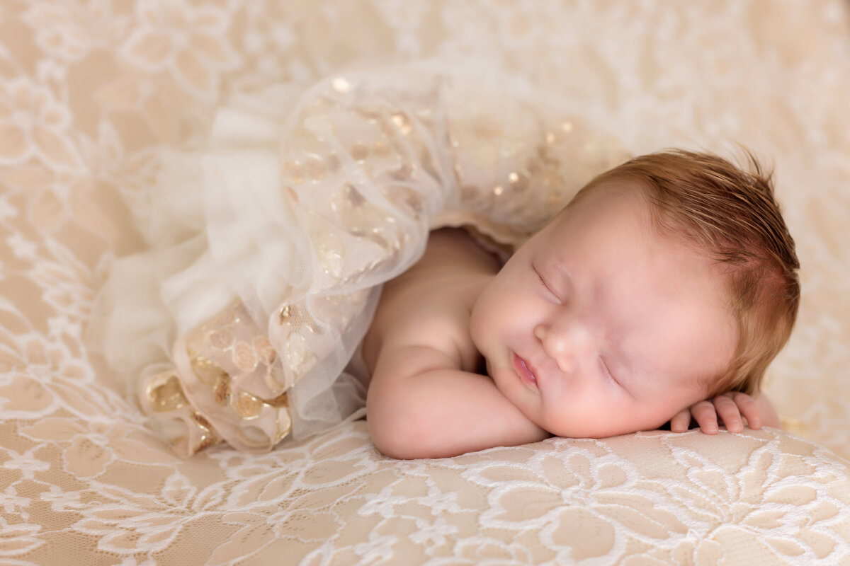 Newborn Photographer, a baby lays on a bedsheet covered in tule