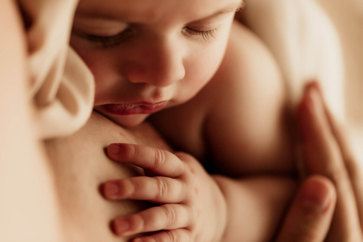 Baby girl rests her hand on her mothers chest while sleeping.