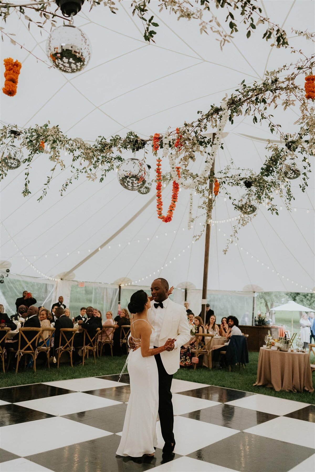 Bride and Groom dancing in a tented wedding on a black and white dance floor under disco balls and greenery and garlands at Ankony Carriage House in the Hudson Valley