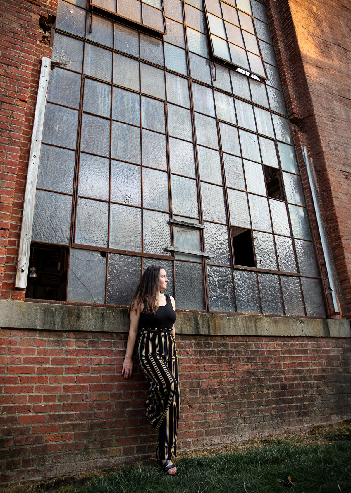 A Maryland entrepreneur leans against an industrial building in Clipper Mill for a photograph with Ingrid Berrios Photography.