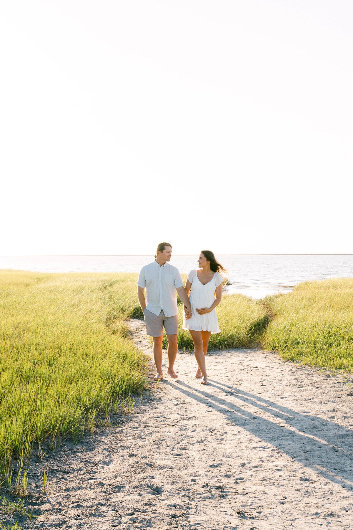 Couple walking at the beach, woman holding her pregnancy bump