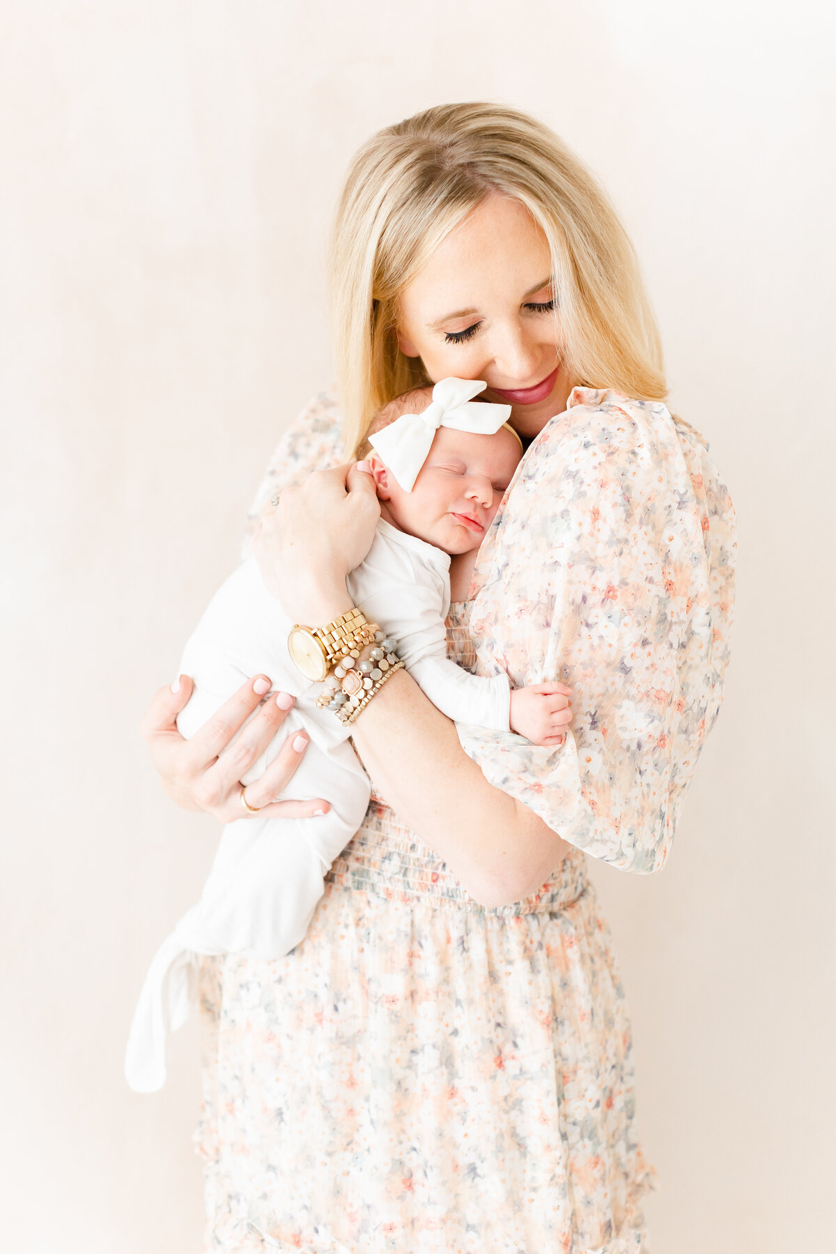 A photo of a mother snuggling her baby girl in a pink floral dress in front of a pink hand-painted canvas by Washington DC Maternity photographer