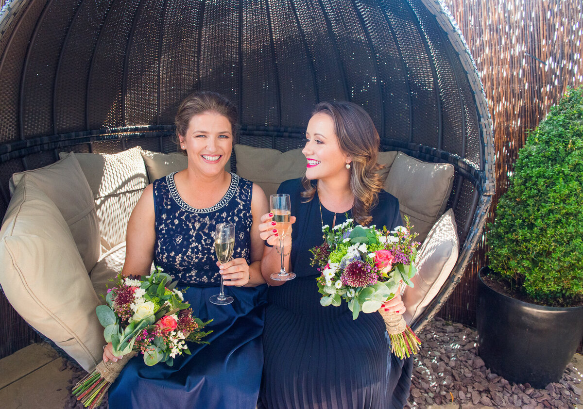 Gay brides wearing blue dresses, with champagne and colourful flower bouquets