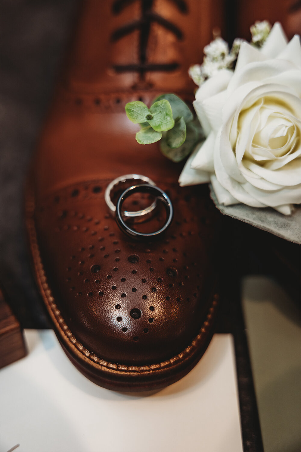 Wedding rings resting on top of brown leather shoe at a sage green mountain wedding.