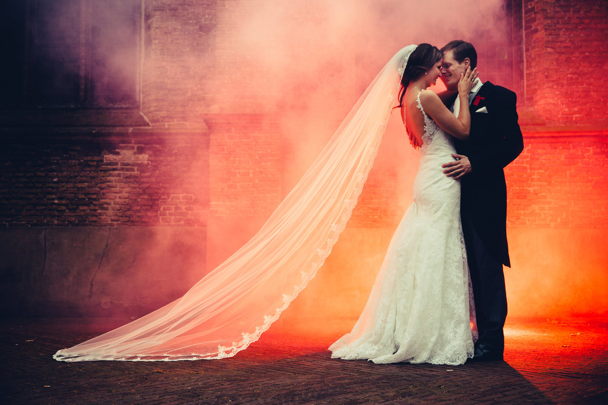 Bruidspaar met rode rookbom voor kerkmuur. Smokebomb. Copyright Nanda Zee-Fritse | FOTOZEE