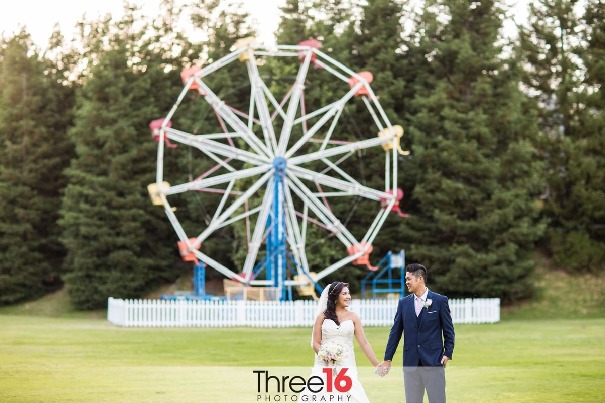 Bride and Groom hold hands and look at each other in front of the Calamigos Ranch Ferris Wheel