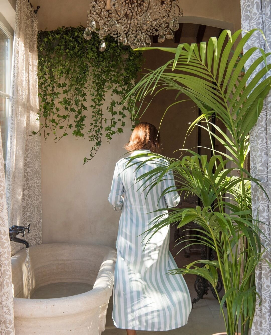 A woman in a sage green and white striped kaftan walks beside a freestanding stone bathtub at Borgo Santo Pietro