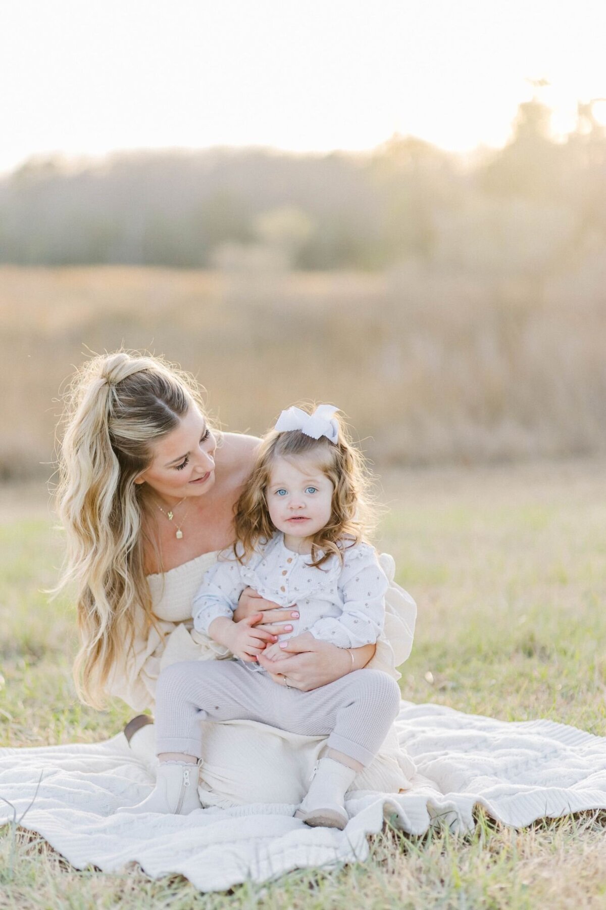 Woman sits with daughter on grass field.