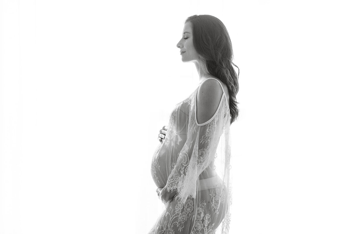 maternity boudoir portrait of mom wearing a sheer lace dress in nashville photographer’s studio