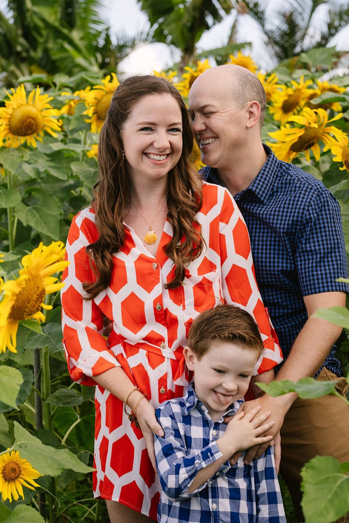 family of three pose in the sunflower field at keiki and plow