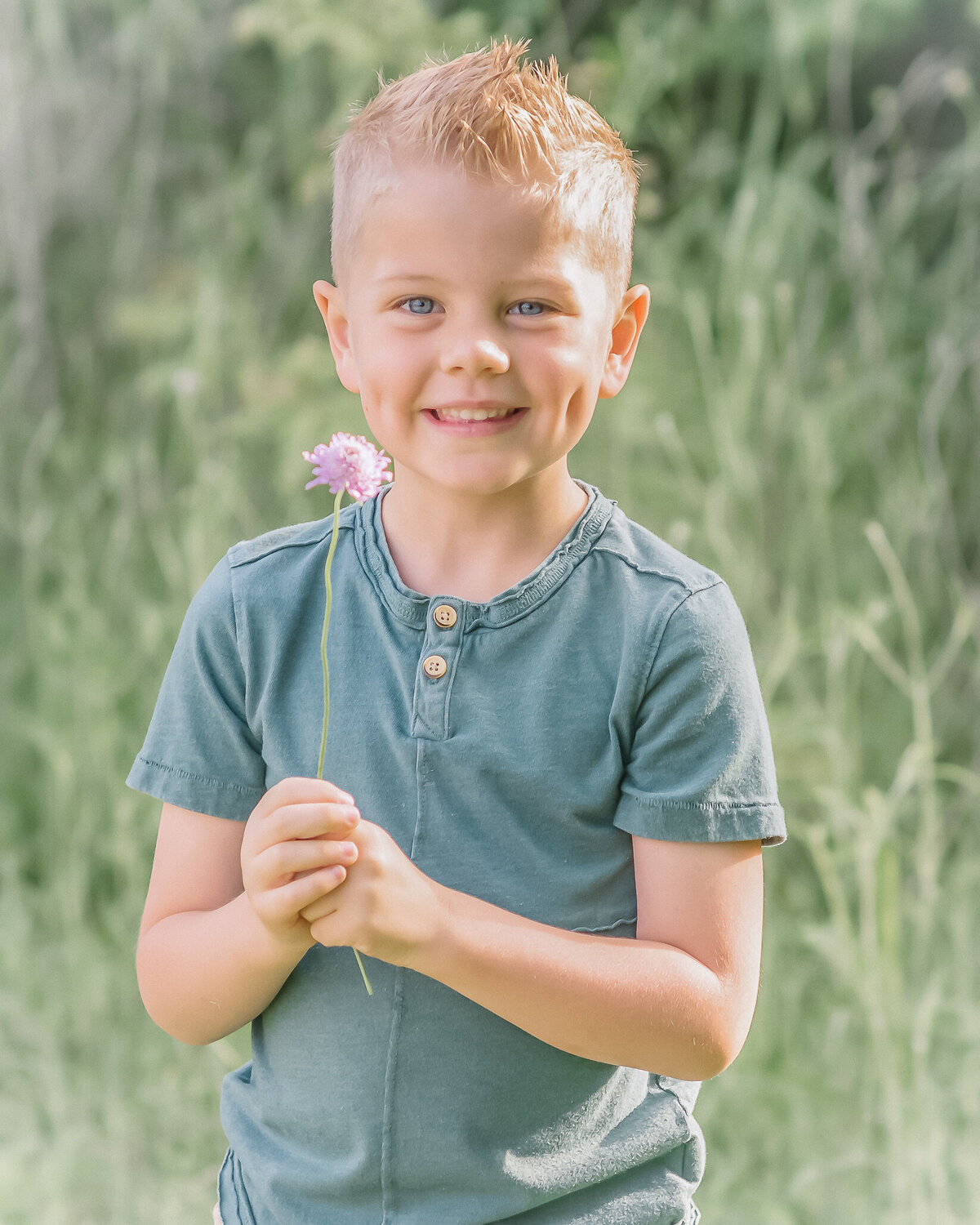 super cute little boy smiling and holding a flower outdoors