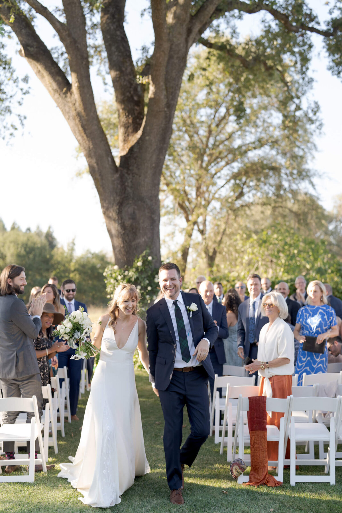 A happy married couple hold hands and walk back up the aisle. Photographed in Sonoma County by wedding photographer Robin Jolin.