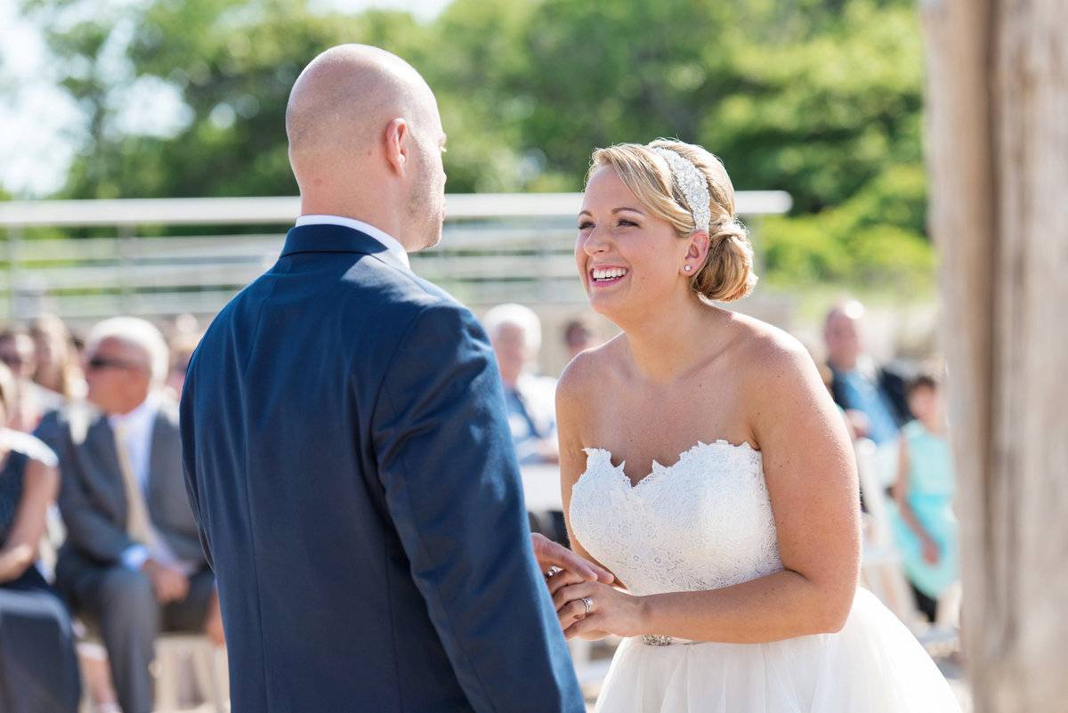 bride smiling at groom during wedding ceremony on the beach at Pavilion at Sunken Meadow