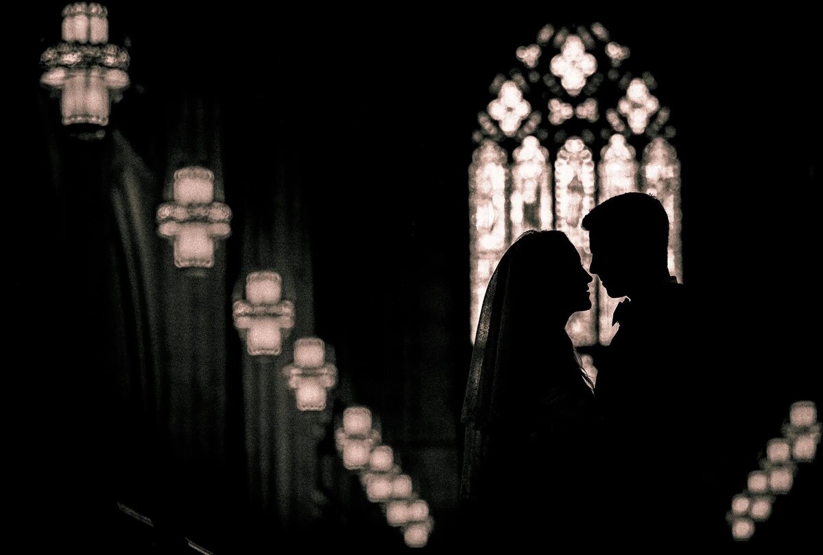Silhouette of a couple sharing a tender moment with the warm glow of chandeliers and stained glass windows in the background.