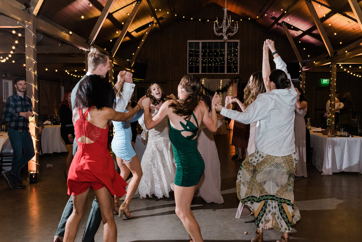 denver wedding photographer photographs reception with guests dancing together in a gorgeous denver wedding venue decorated with white linen and twinkle lights