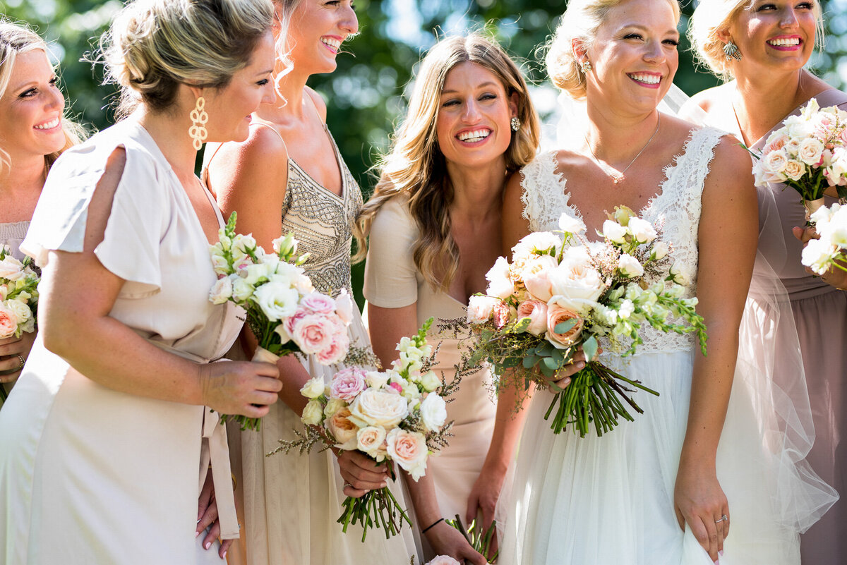 Bride and her bridesmaids laugh during their portraits before wedding ceremony